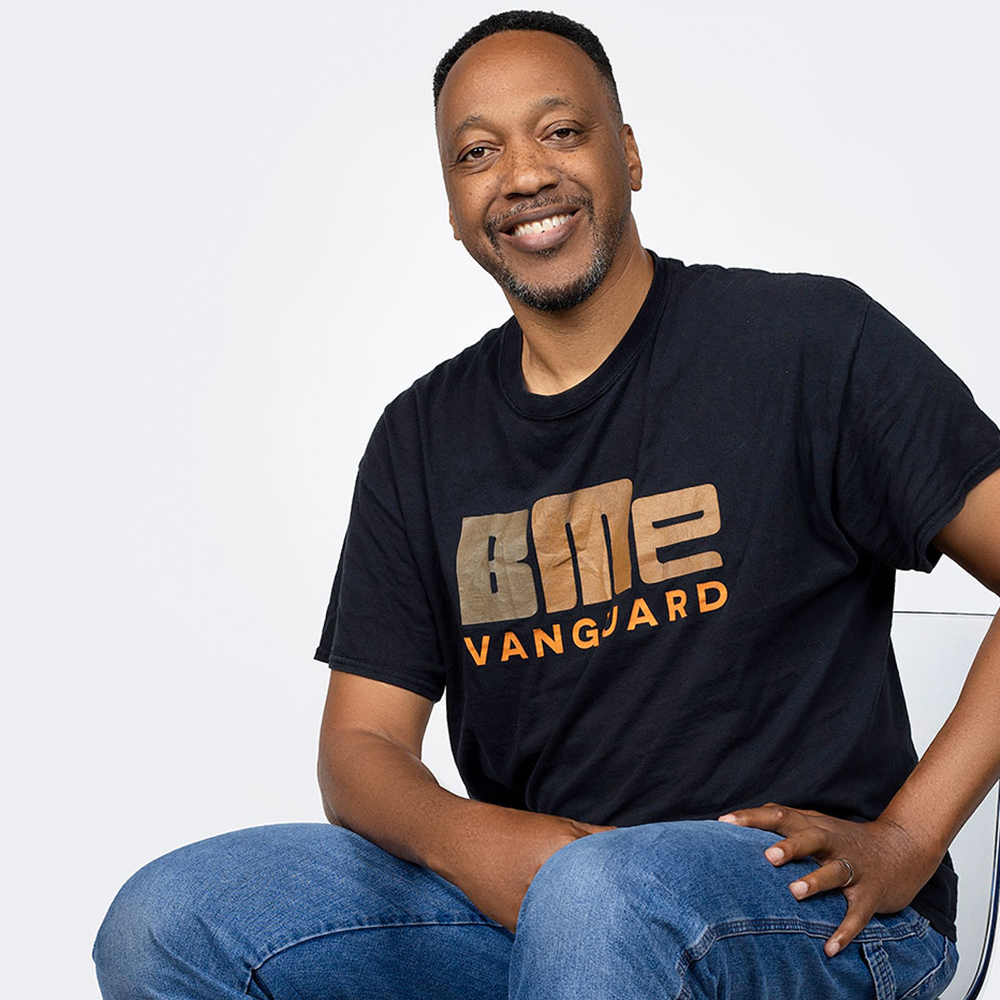 A man sitting on a chair wearing a t - shirt that says gme vangard.