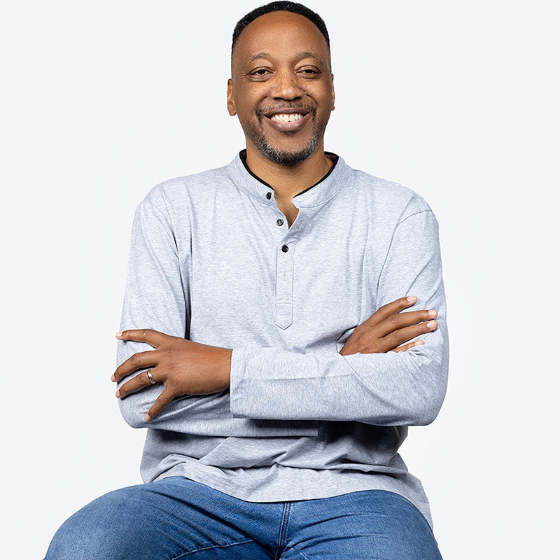 A smiling man in a gray shirt and jeans sitting on a chair. A smiling man in a gray shirt and jeans sitting on a chair.