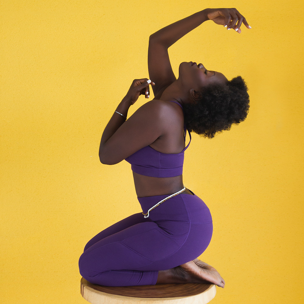A woman in purple yoga pants is posing on a stool.