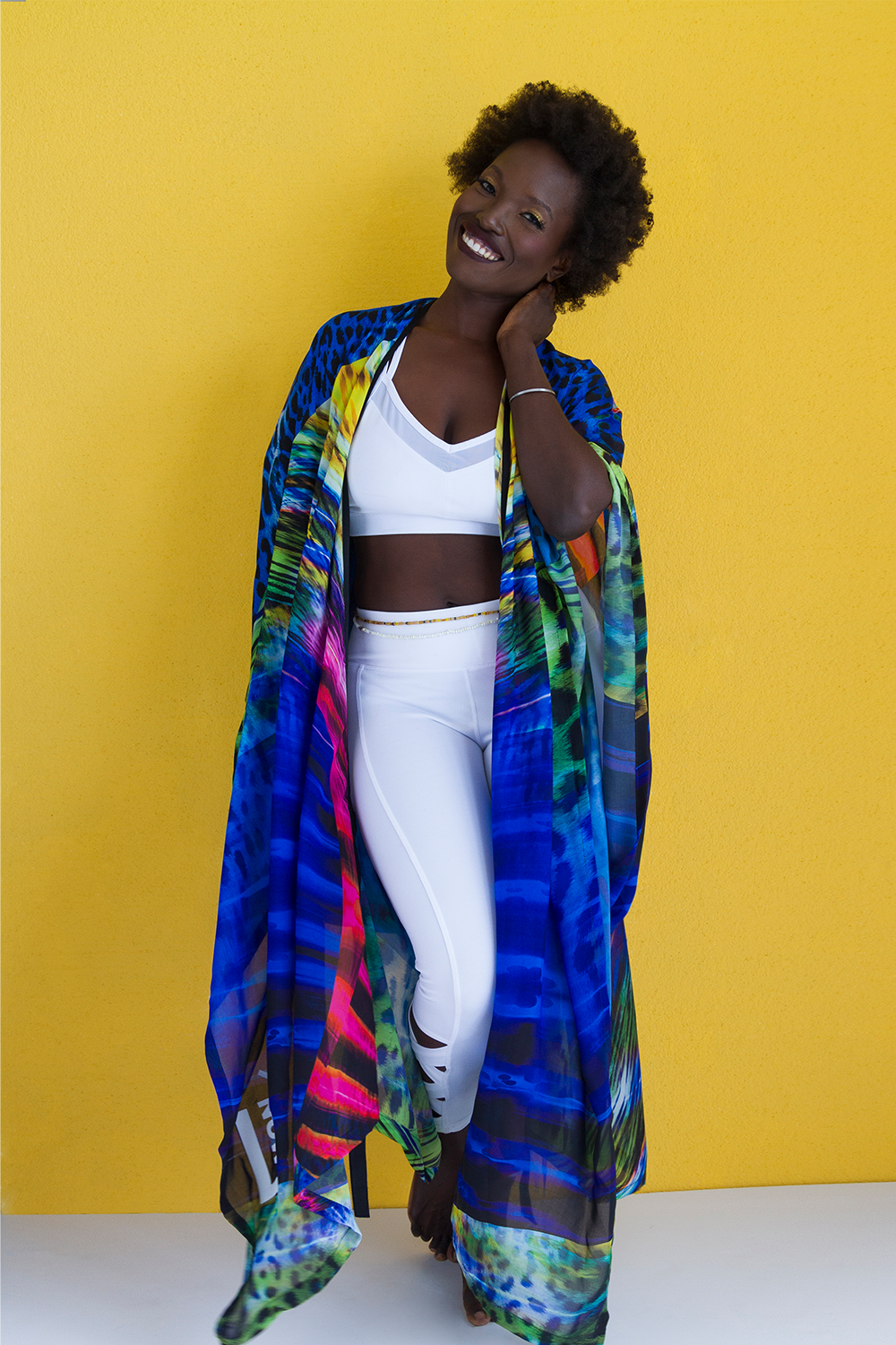 A woman wearing a colorful kaftan posing in front of a yellow wall.