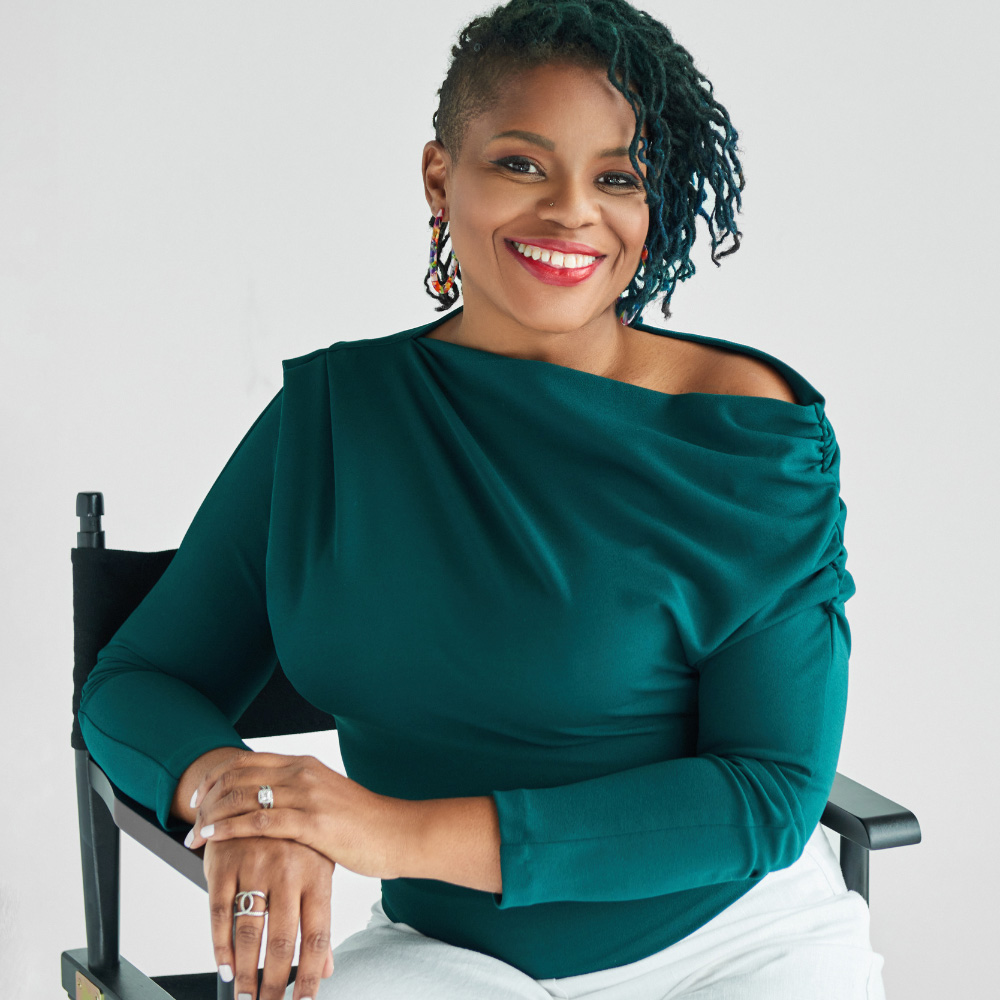 A woman in a green top and white pants sitting in a chair.