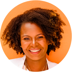 A woman with a curly afro smiles in front of an orange wall.